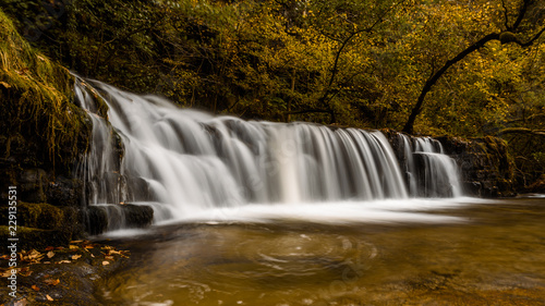 Waterfall Ddwli Isaf near pontneddfechan in the brecon beacons national park, Wales. It is autumn, and golden leaves are all around. Long shutter speed for a smooth effect on the water