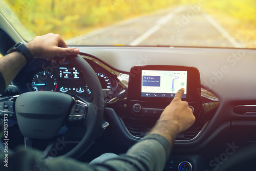 Male driver using dashboard screen maps while driving on road in autumn warm colors