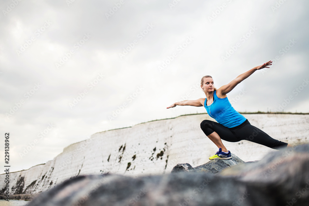 Young sporty woman runner with earphones stretching on the beach outside.