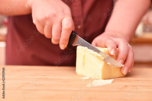 Female hands and knife cut fresh parmesan cheese on a cutting board. Close-up