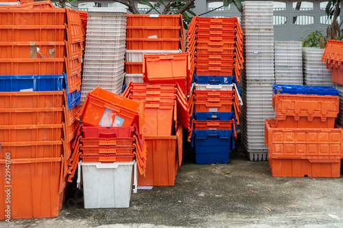 Stacked of old plastic basket and boxes in orange, blue and white color on concrete floor with tree and concrete fence in background