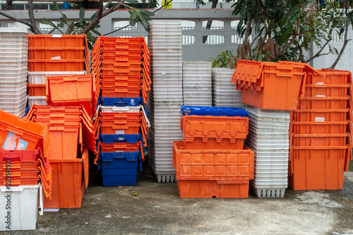 Stacked of old plastic basket and boxes in orange, blue and white color on concrete floor with tree and concrete fence in background © samrit