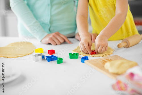 family, cooking and people concept - mother and little daughter with molds making cookies from dough at home kitchen