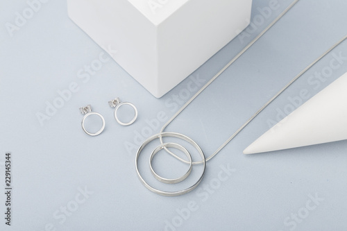 Minimalist geometric silver necklace and circle stud earrings on gray background