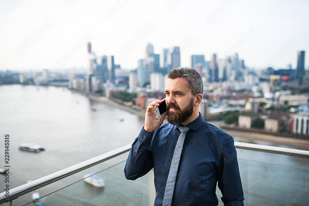 A portrait of businessman with smartphone standing against London view panorama. A portrait of businessman with smartphone standing against London view panorama.