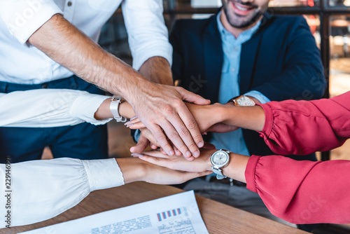 cropped shot fo business team holding hands at workplace in office