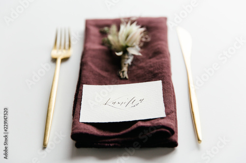 Table setting with golden colored cutlery styled with a purple linnen napkin, boutonniere and handwritten place card.