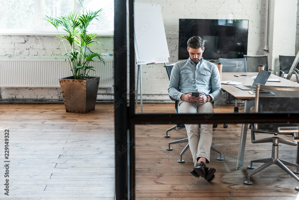 handsome young businessman using smartphone while sitting at workplace handsome young businessman using smartphone while sitting at workplace