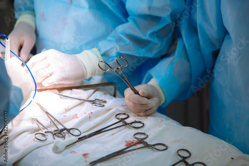 Close-up surgical instruments on a medical table in a clinic during surgery. Metal sterile scissors, clamp, surgical needle at the table or in doctor hand. The concept of health, tools.