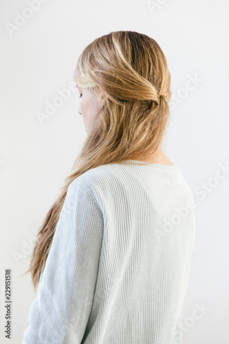 A woman with long straight dark blonde hair wearing a light cotton knitwear seen from the back.