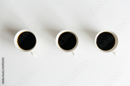 Three cups of black coffee on a white table seen from above.