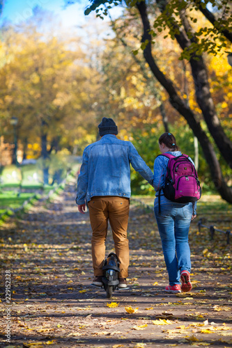 A man on a monowheel and a woman are walking on a sunny day in an autumn park