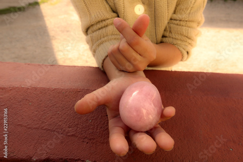 Ein Mädchen hält auf einer Hand ein Rosenquarz, während sie  Koreanisches Herz Finger Zeichen macht.