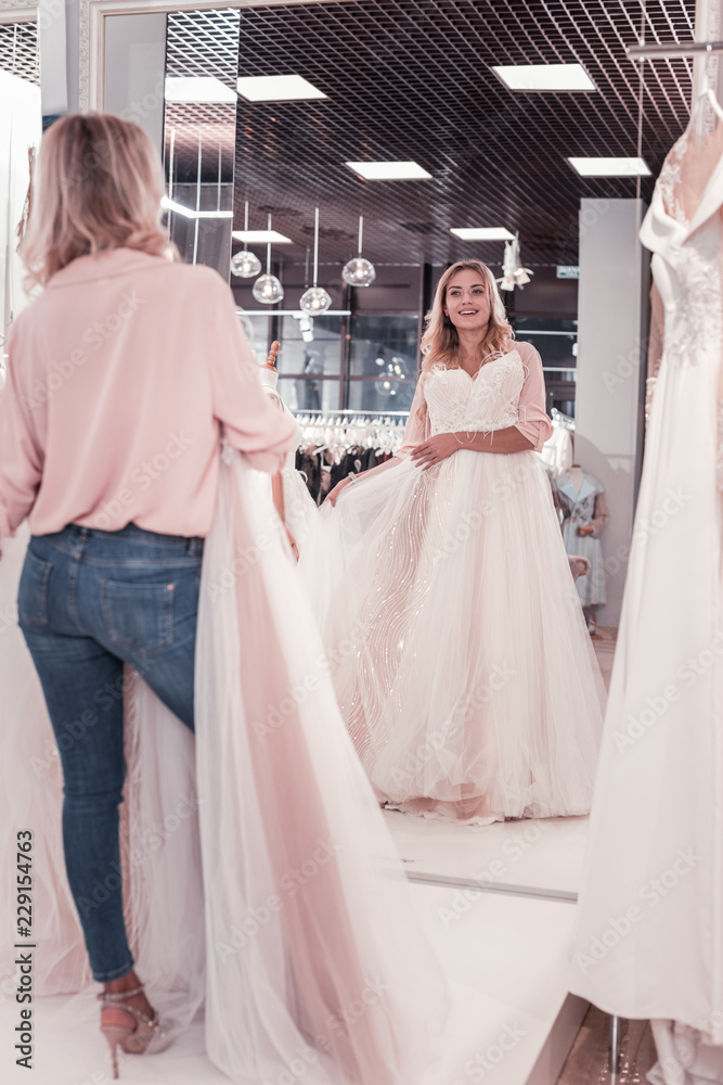 Full length look. Positive beautiful woman standing in front of the mirror while looking at herself in wedding dress