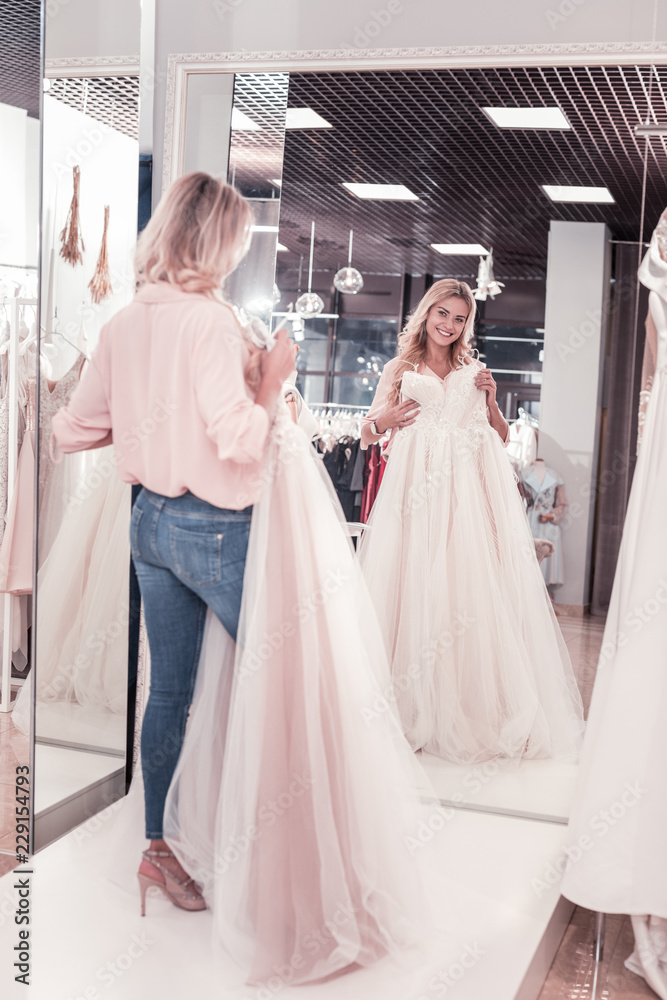 Fototapeta premium The most beautiful bride. Joyful delighted woman looking at the wedding dress while standing in front of the mirror