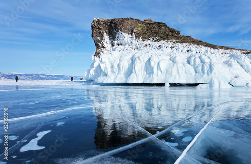 Baikal Lake in February cold day. Tourists travel on the ice near the Cape  Horin-Irgi (Kobylia Golova) of Olkhon Island. Beautiful winter landscape with reflection of icy rock in blue mirror ice photo