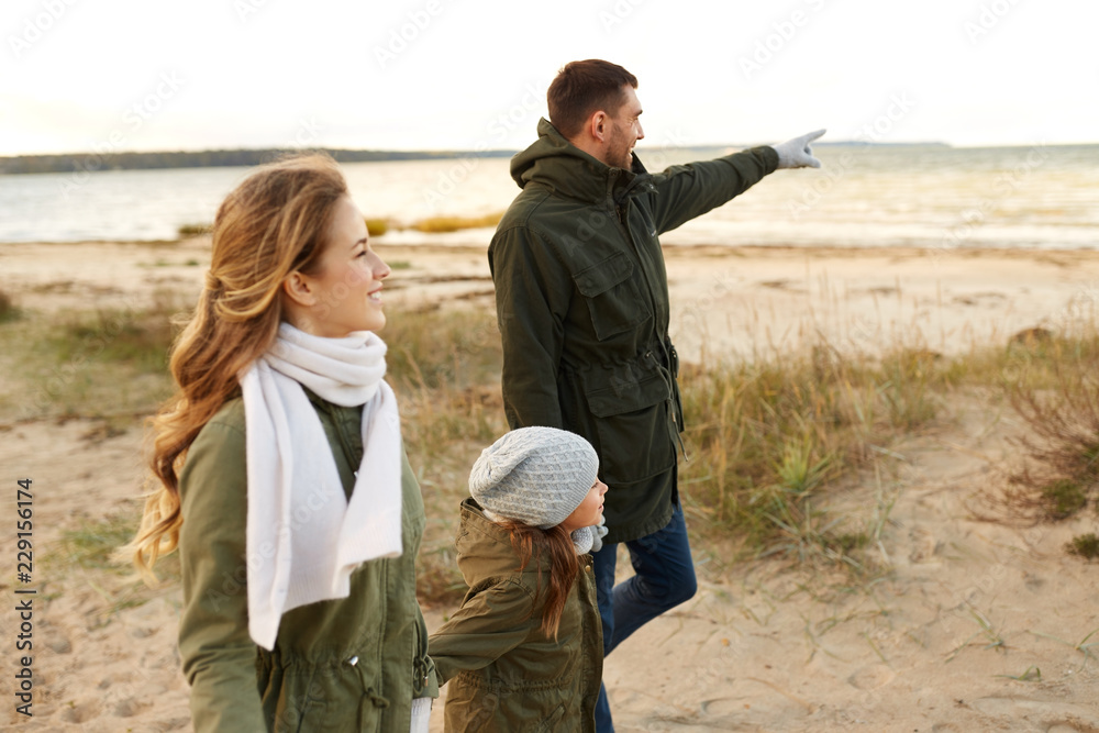 Fototapeta premium family, leisure and people concept - happy mother, father and little daughter walking along autumn beach