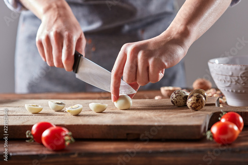 Vászonkép Boiled quail eggs cut female hands on a wooden board on a table with tomatoes and spinach