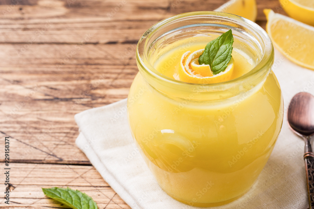 Homemade lemon curd in glass jars with fresh lemons, rustic wooden background copy space Homemade lemon curd in glass jars with fresh lemons, rustic wooden background copy space