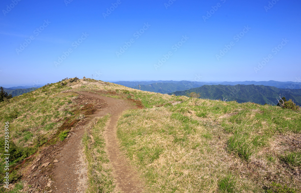 Dirt trail to top of mountain under vibrant blue sky on sunny day Dirt trail to top of mountain under vibrant blue sky on sunny day