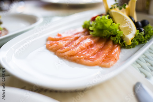 sliced smoked salmon served with lemon slices on white plate