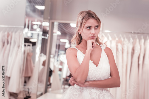 Best wedding dress. Beautiful pensive bride coming to the wedding boutique while looking for the best wedding dress