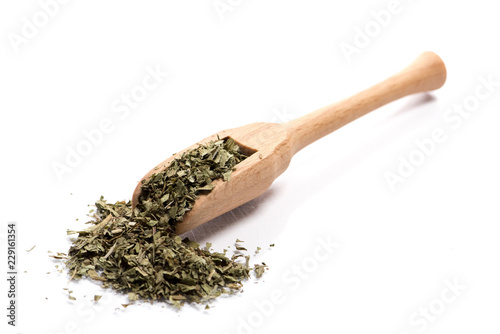 Close-up of pile of dried herbs, devisil leaves in a wooden spoon on white background
