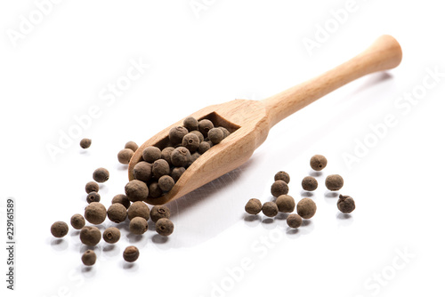 Close-up of pile of Pimento, Bahar seeds spice in a wooden spoon on white background