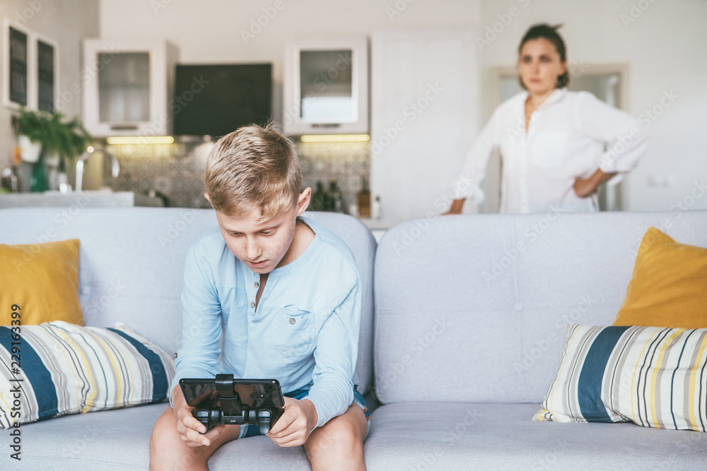 Mother unhappy with teenager son who spent his free time with electronic devices and games. Relationships teenager vs parents concept image.