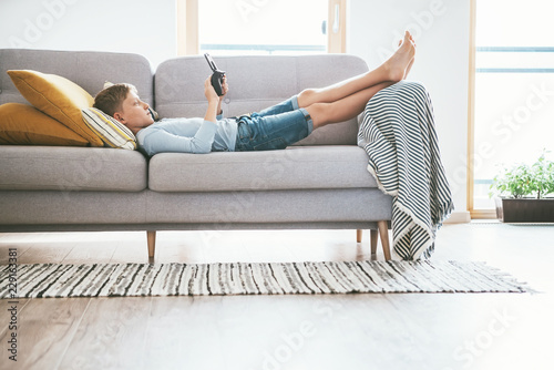Fotografie Boy plays with electronic devices - gamepad connected with smartphone lying on the cozy sofa in the home living room