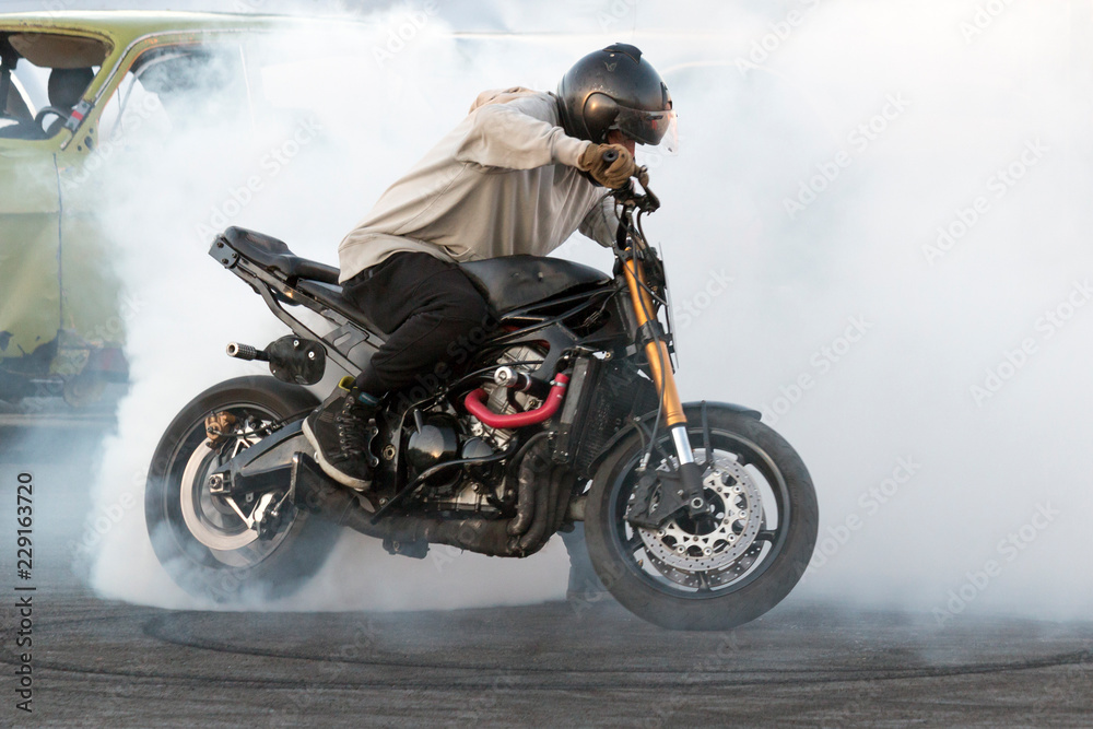 Biker burning tires and creating smoke on motorcycle in motion