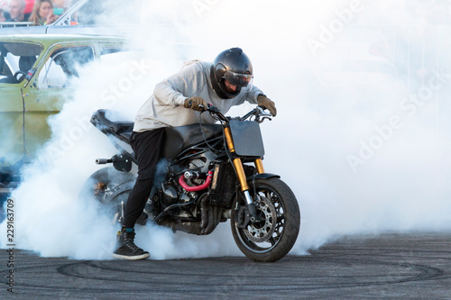 Motorcyclist staying on the bike, burning tire and creating smoke on the moto show