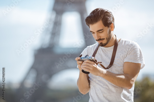 Paris Eiffel Tower tourist with camera taking pictures in front of the Eiffel tower, Paris, France. Young professional photographer handsome man in casual clothes outdoors in Europe.