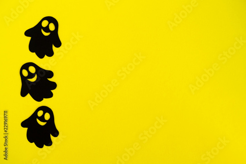 Holiday decorations for Halloween. Three black paper ghosts on a yellow background, top view.