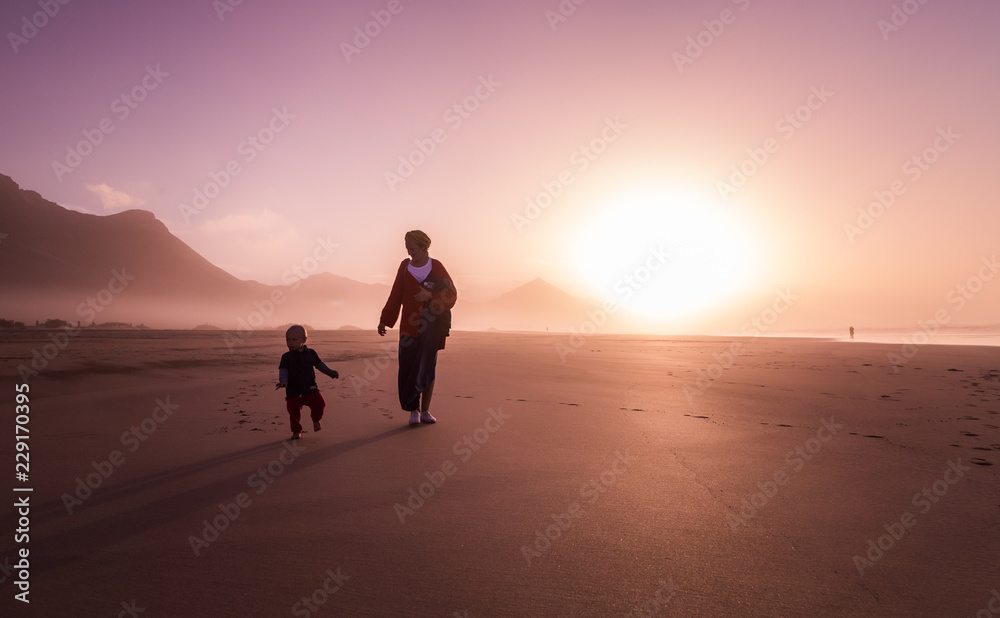 Silhouette of young mother with her little child walking on sunshine in Cofete.