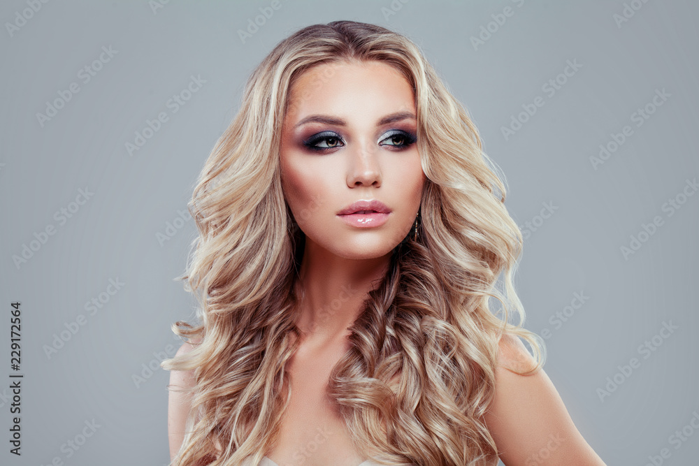 Blonde beauty. Young perfect woman with long curly hair and makeup on blue background
