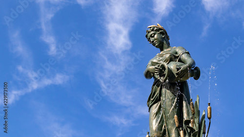 Female bronze statue with cloudy blue sky background  public gardens  autumn sunshine.