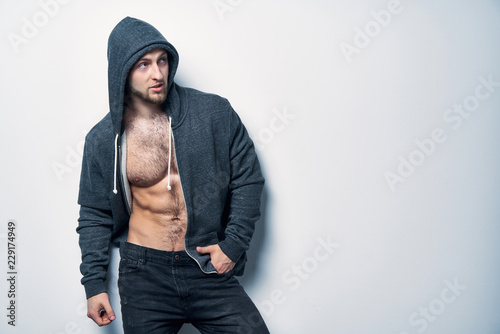Photography Brutal naked muscular man dressed in a grey hoodie posing by white wall looking