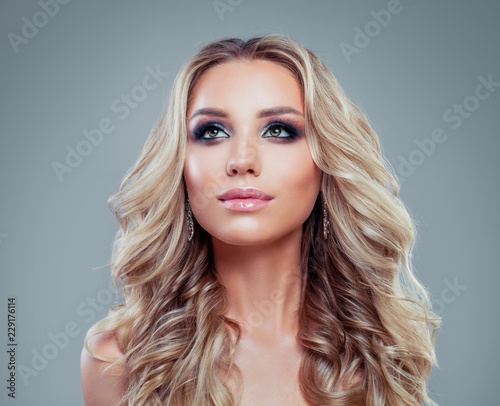 Perfect blonde woman with long curly hair and makeup looking up