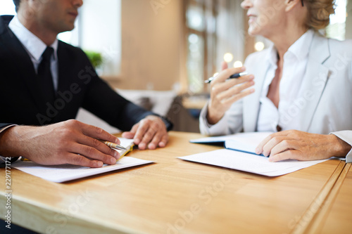 Close-up of business people sitting at the table with documents and discussing business contract