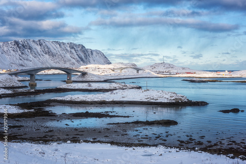 Beautiful winter daytime landscape in Lofoten Islands. Snowy rocky mountains, bridges between islands, blue cloudy sky and reflection in the water, Norway © larauhryn