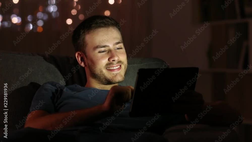 Man watching media with a tablet in the night sitting on a couch in the living room at home Man watching media with a tablet in the night sitting on a couch in the living room at home