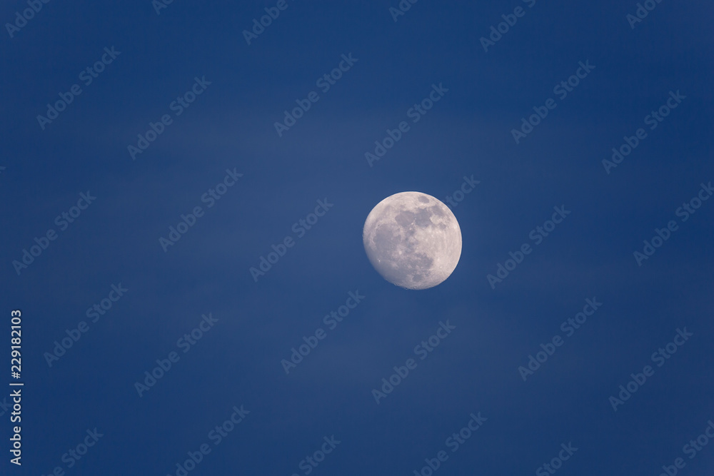 Full moon in daytime in blue hour with soft white clouds 