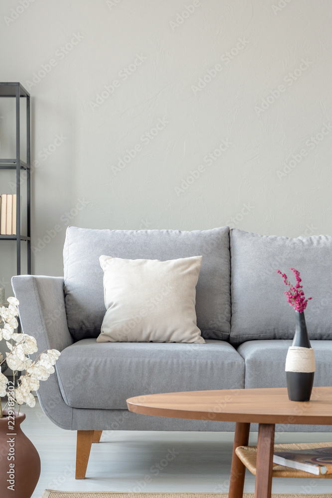 Fototapeta premium Heather in vase on the wooden table next to comfortable grey couch in monochromatic living room, real photo with copy space on the wall