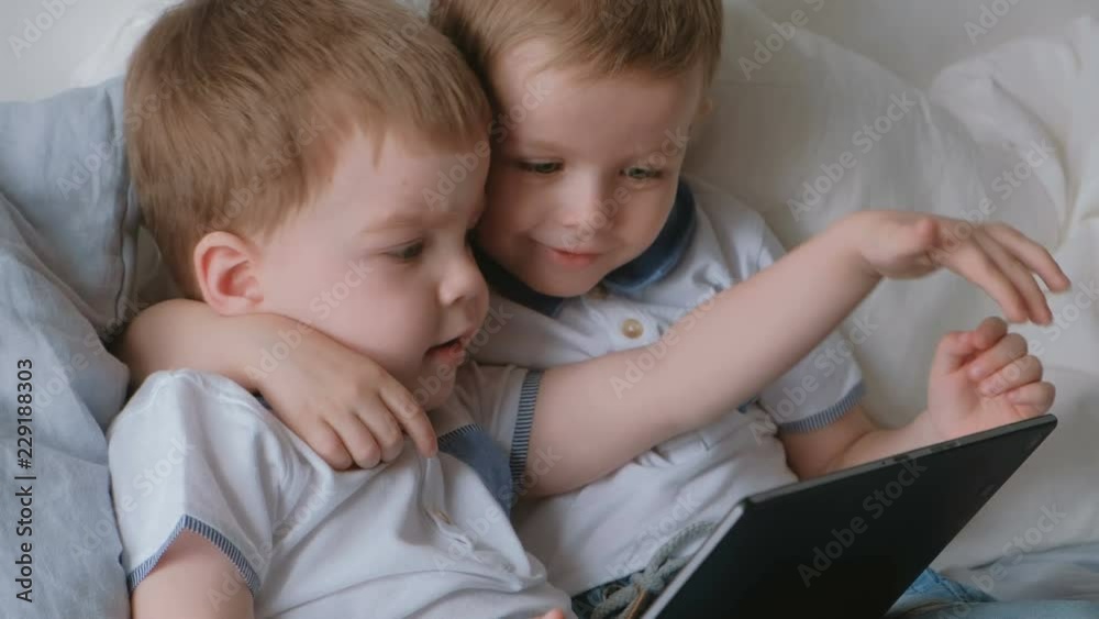 Kids with tablet. Two boys twins toddlers looking cartoon at tablet lying on the bed. Kids with tablet. Two boys twins toddlers looking cartoon at tablet lying on the bed.