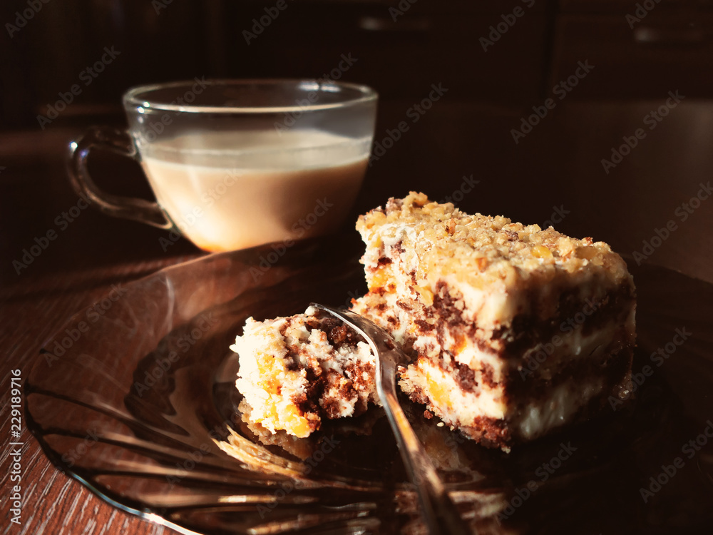Piece of chocolate cake on a plate and a cup of coffee with milk on a dark wooden table in the kitchen Piece of chocolate cake on a plate and a cup of coffee with milk on a dark wooden table in the kitchen