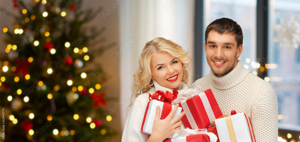 holidays and people concept - happy couple with gifts at home over christmas tree lights background holidays and people concept - happy couple with gifts at home over christmas tree lights background