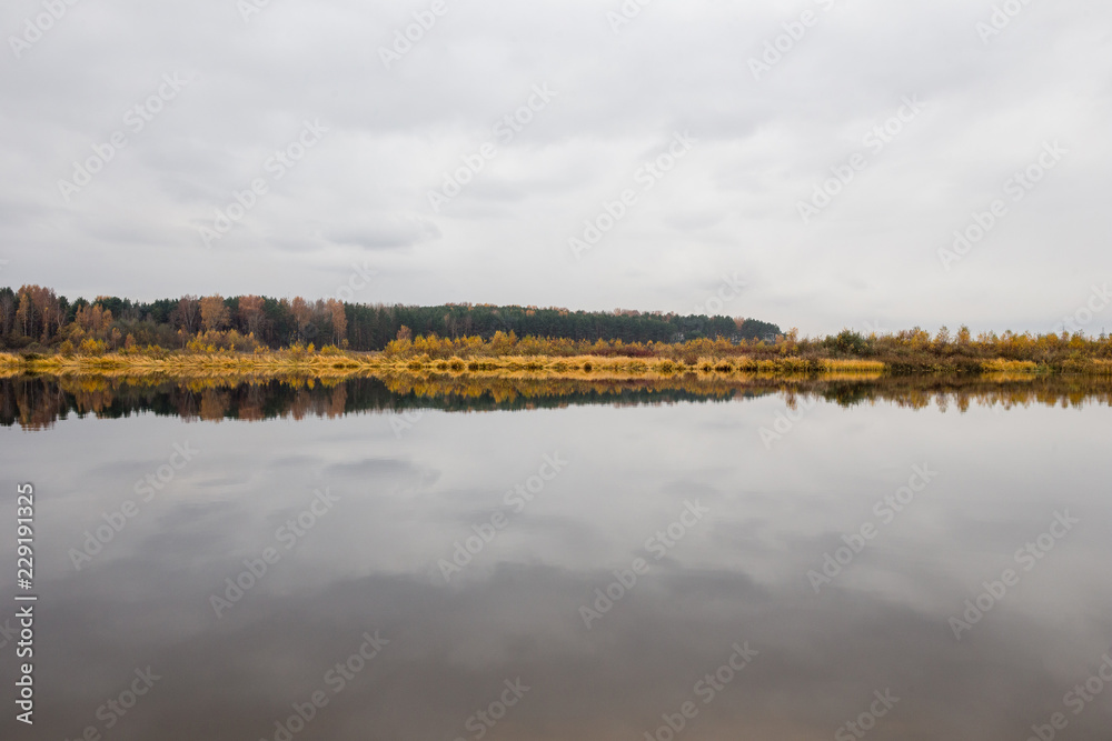 The autumn forest is reflected in the calm water of the river.