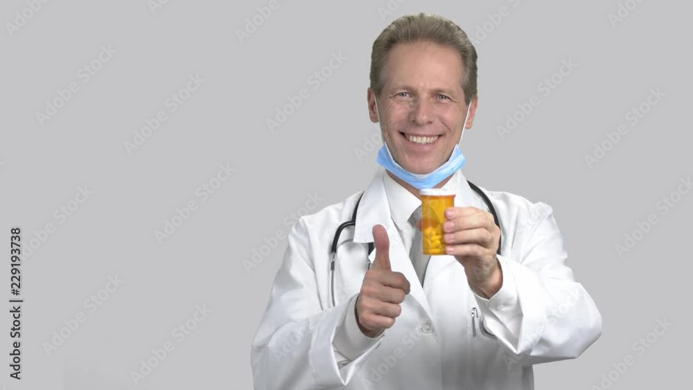 Mature handsome man recommending can of pills. Holding orange can of pills and thumb up, grey isolated background. Mature handsome man recommending can of pills. Holding orange can of pills and thumb up, grey isolated background.