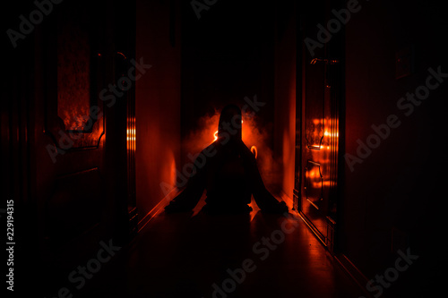 Creepy silhouette in the dark abandoned building. Horror Halloween concept. Dark corridor with silhouette of horror person standing in center. Toned light and fog on background. Selective focus